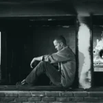 A man sits alone, back against a wall, suffering from depression