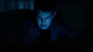 An angry young man looks at his cell phone in the dark