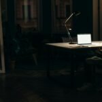 A man sits alone at his desk at night, looking at his phone